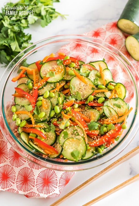 Asian cucumber salad in a large glass bowl topped with toasted sesame seeds and fresh cilantro