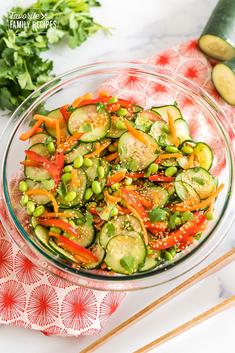 Asian cucumber salad in a large glass bowl topped with toasted sesame seeds and fresh cilantro