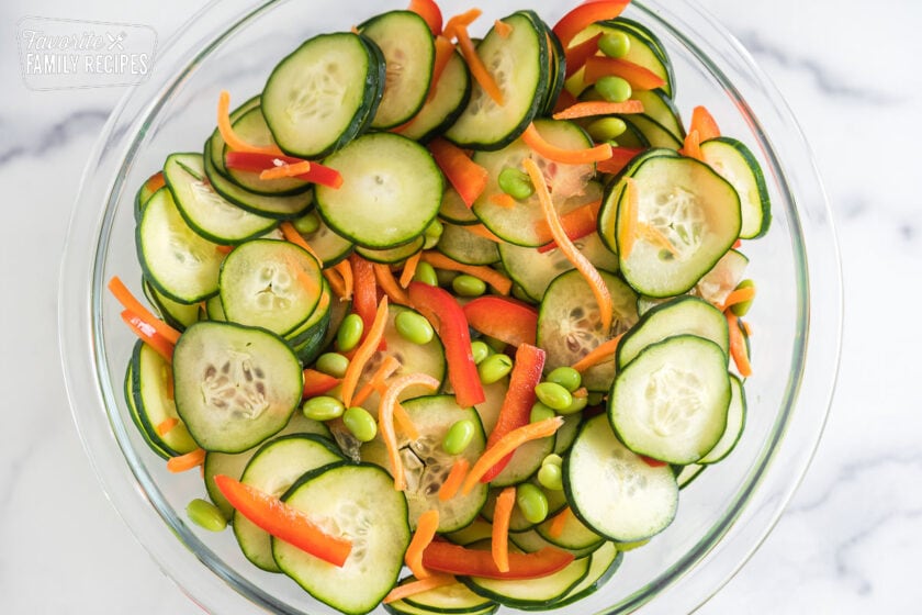 Sliced cucumbers, carrots, red peppers, and edamame in a large glass bowl