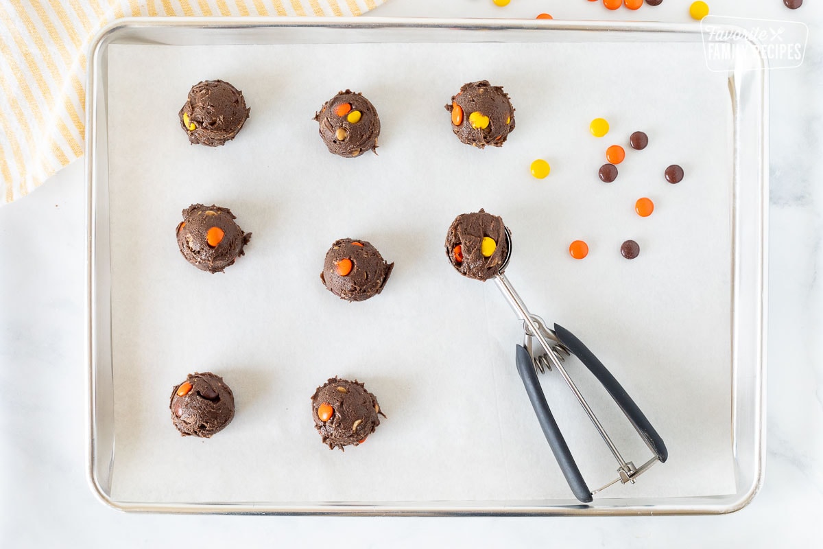 Balls of Reeses Pieces Cookie dough on a cookie sheet next to a cookie scoop.