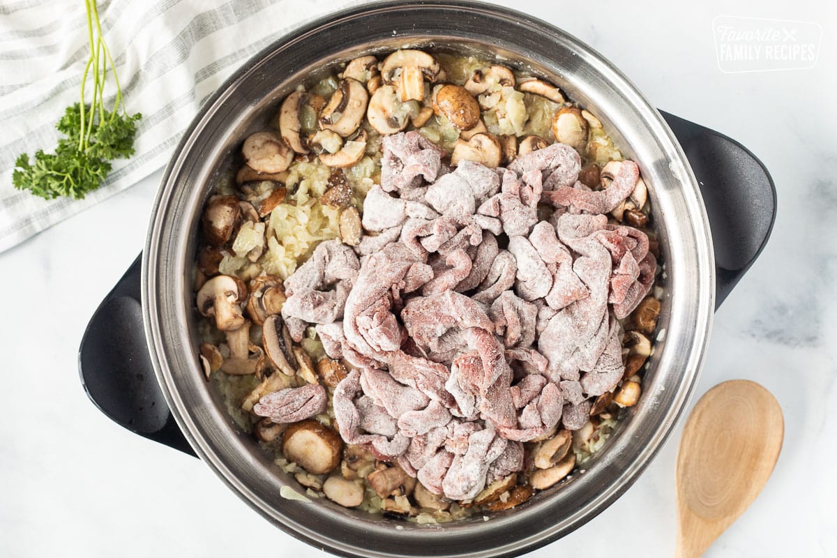 Skillet with onions and mushrooms with flour coated beef for Easy Beef Stroganoff.