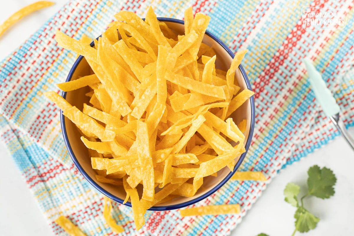 Bowl of homemade salted Tortilla Strips with tongs on the side.