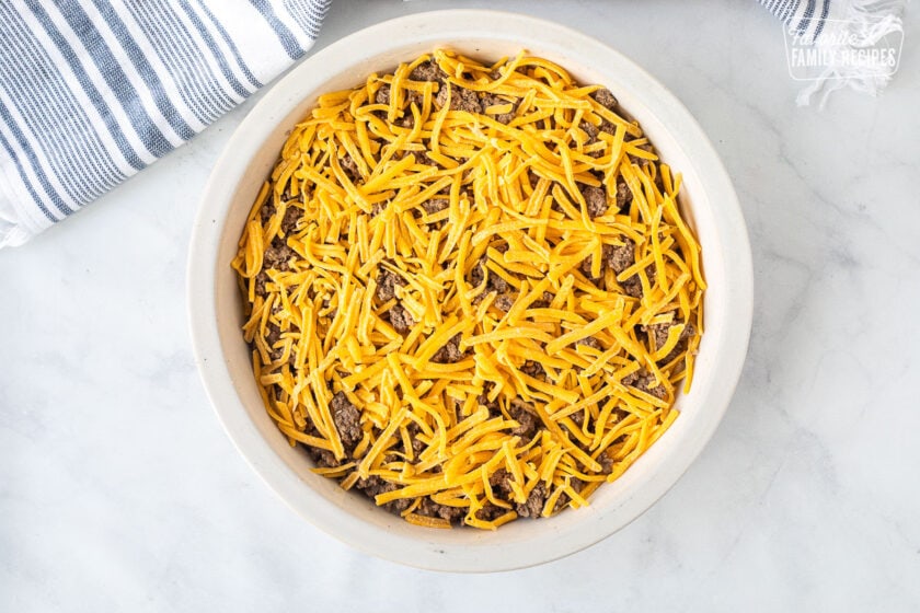 Pie Plate with ground beef and shredded cheddar cheese for Cheeseburger Pie.
