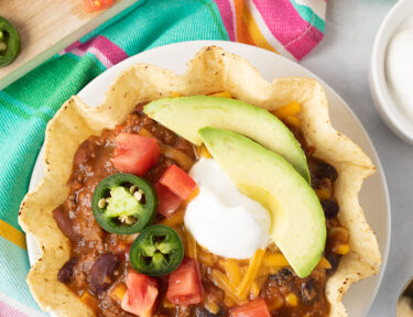 Tostada bowl of Mexican Chili with cheese, sour cream, jalapeños, avocado and tomatoes.