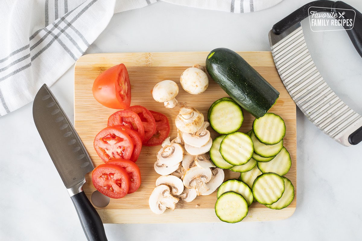 Cutting board with sliced tomatoes, mushrooms and zucchini for Healthy Pizza.