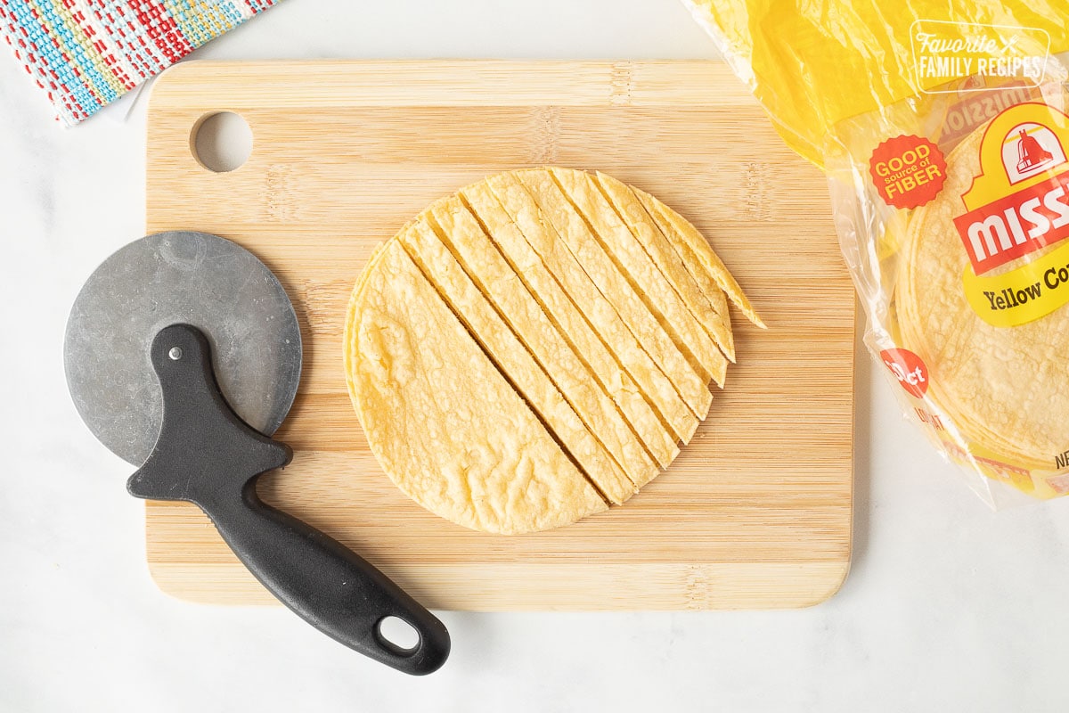 Cutting board with a pizza cutter and sliced corn tortillas for Tortilla Strips.