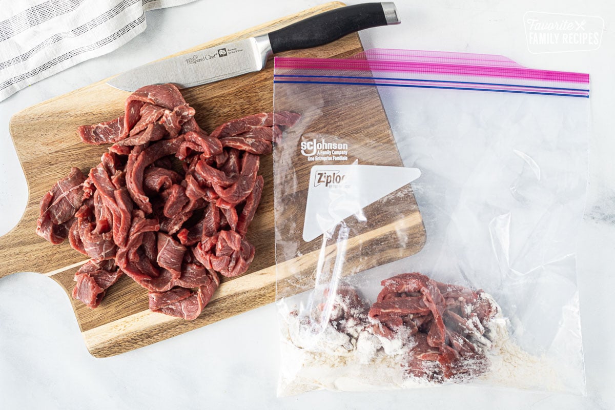 Sliced beef on a cutting board for Easy Beef Stroganoff. Ziplock bag with flour beef slices.