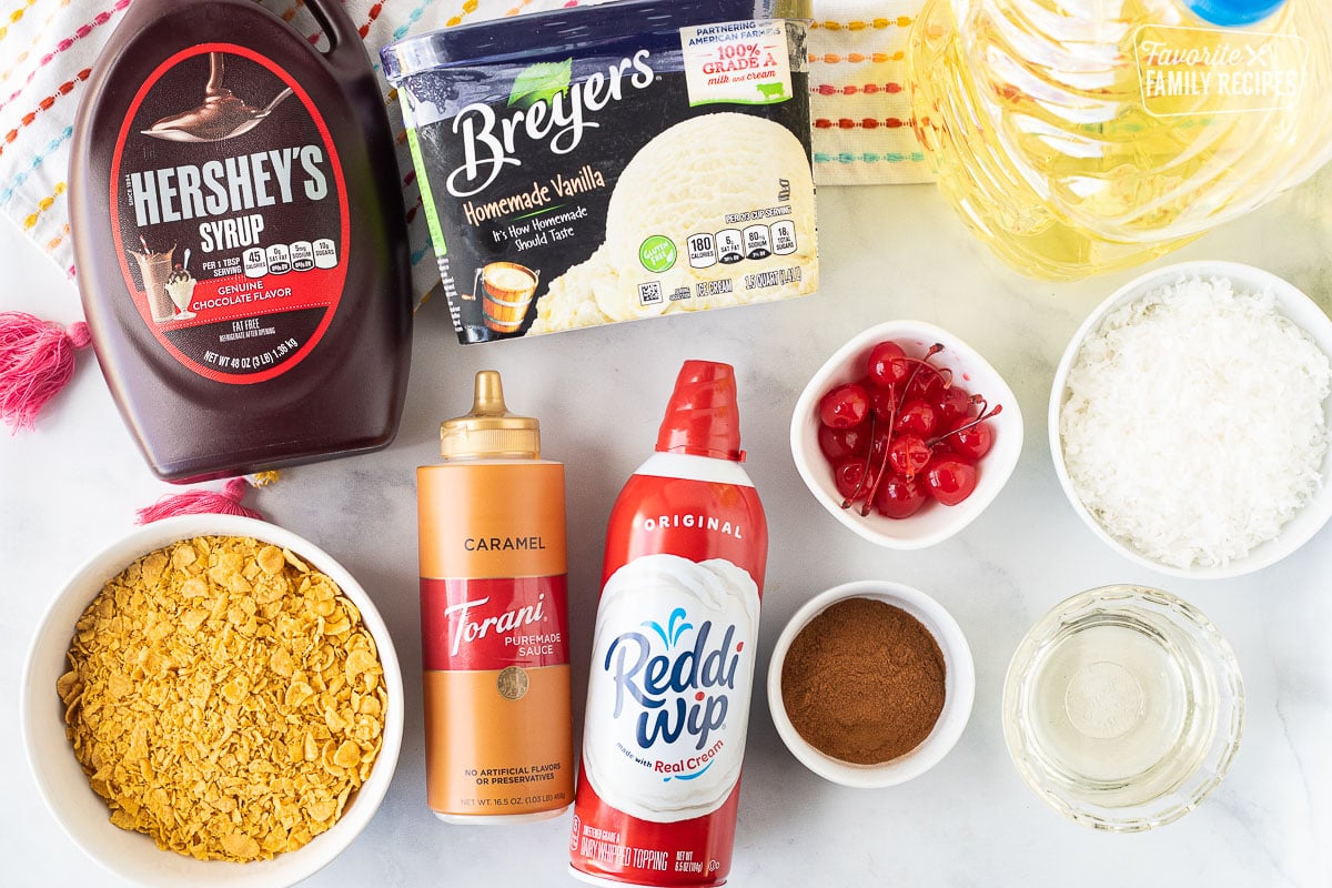 Ingredients to make Fried Ice Cream including ice cream, oil, chocolate syrup, caramel sauce, corn flakes, cinnamon, corn syrup, coconut, whipped cream and cherries.
