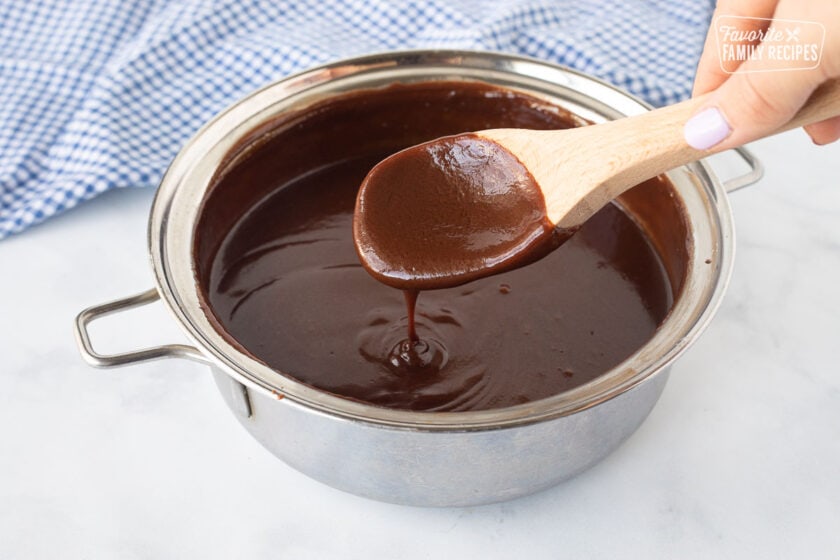 Fudge sauce in a small pan drizzling from a wooden spoon for Banana Split Dessert.