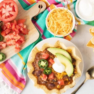 Top view of a garnished tostada bowl of Mexican Chili with sour cream, tomatoes, jalapeños, avocado and shredded cheddar cheese.