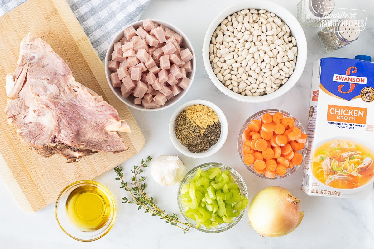 Ingredients to make Ham and Bean soup including ham, ham bone, salt, pepper, beans, chicken broth, carrots, celery, onion, spices, garlic and oil.