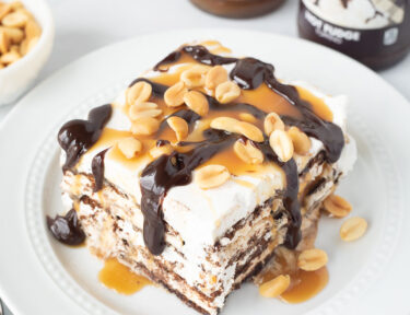 Ice Cream Sandwich Cake slice with hot fudge, caramel drizzling off the sides and peanuts.