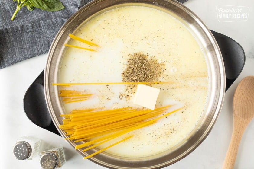 Pot with milk, butter, linguine, basil, salt and pepper for One Pot Creamy Garlic Noodles.