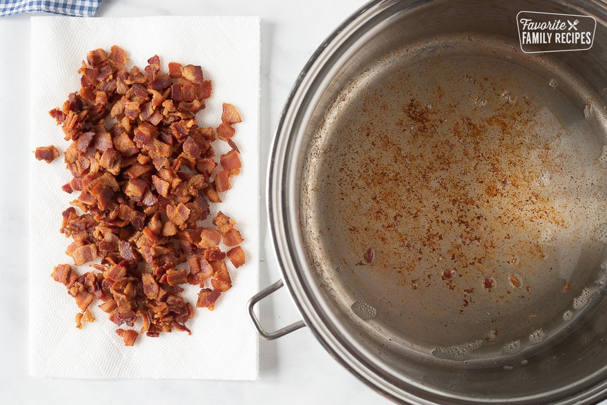 Cooked crispy bacon on a paper towel next to a pot with a little bacon grease for Loaded Potato Soup.