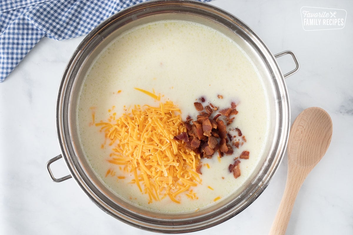 Adding cheese and bacon into Loaded Potato Soup. Wooden spoon on the side.