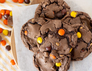 Six Reeses Pieces Cookies on parchment paper with extra candies all around.