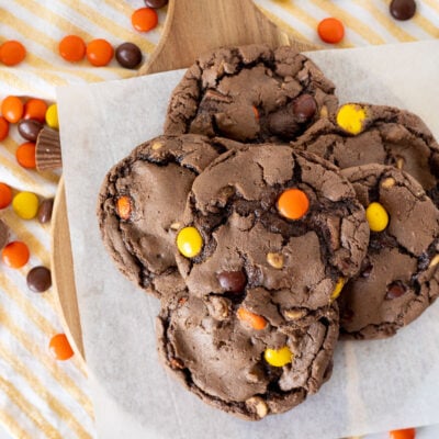 Six Reeses Pieces Cookies on parchment paper with extra candies all around.