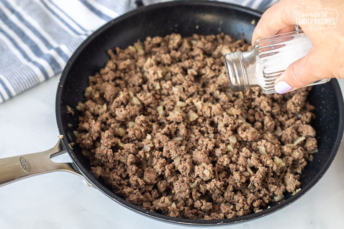 Adding salt to ground beef in a skillet for Cheeseburger Pie.