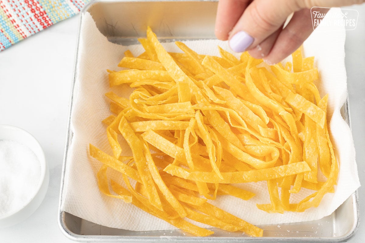 Salting fresh hot Tortilla Strips in a dish lined with a paper towel.