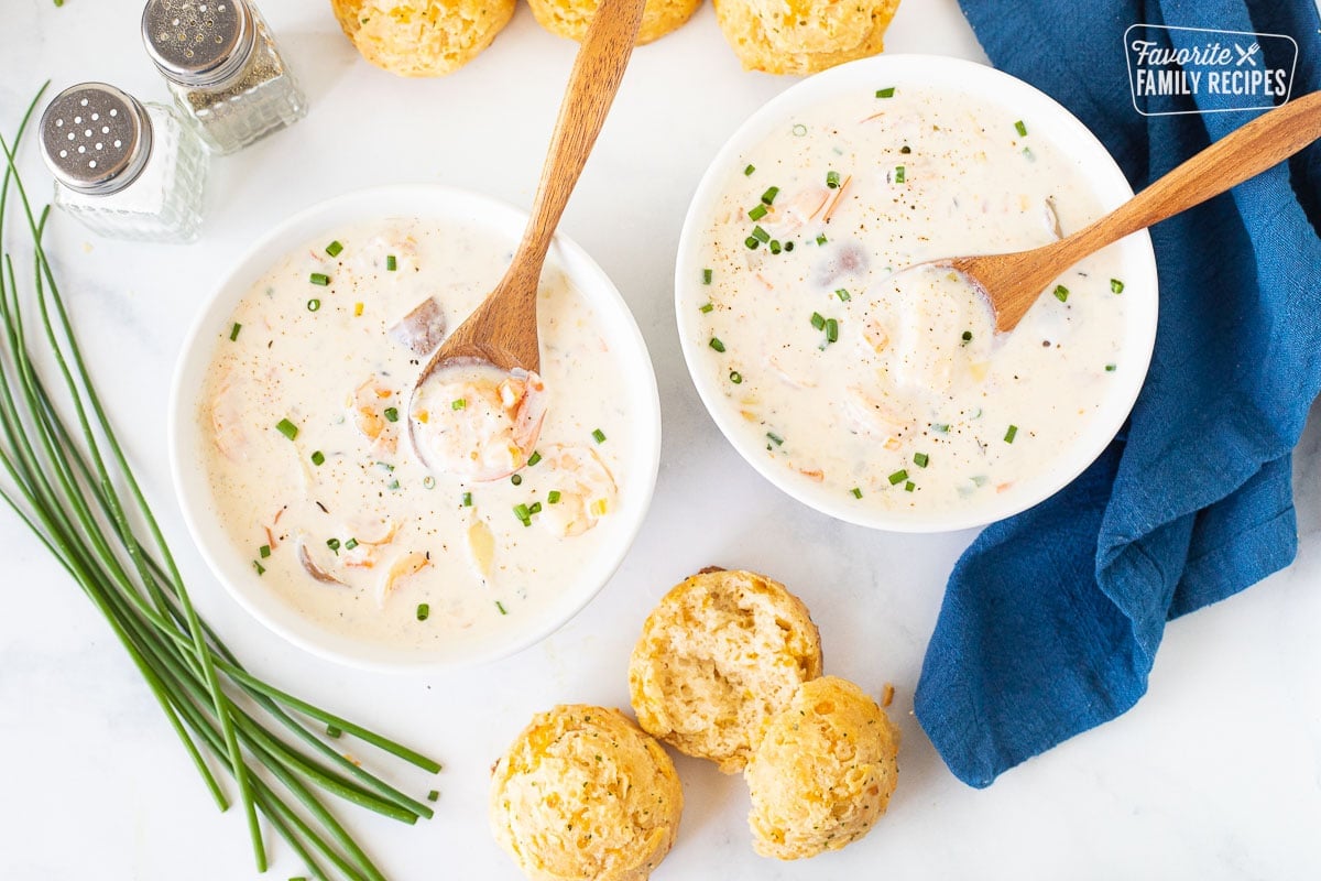 Two bowls of Seafood Chowder with wooden spoons resting in the bowls. Cheddar biscuits on the side.