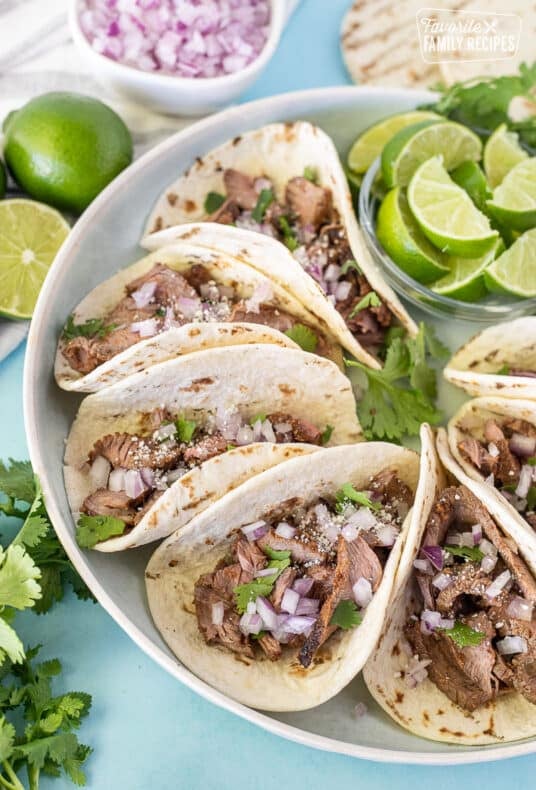 Platter of Steak Street Tacos with sliced lime wedges.