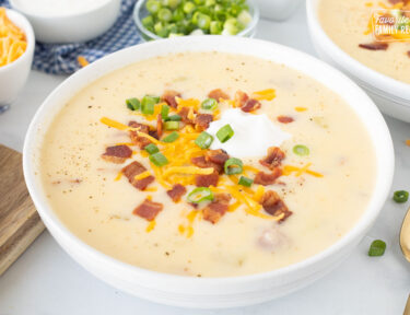 Close up of a bowl with Loaded Potato Soup garnished with cheese, sour cream, bacon and green onions.
