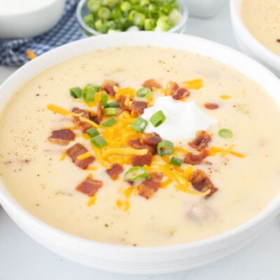 Close up of a bowl with Loaded Potato Soup garnished with cheese, sour cream, bacon and green onions.