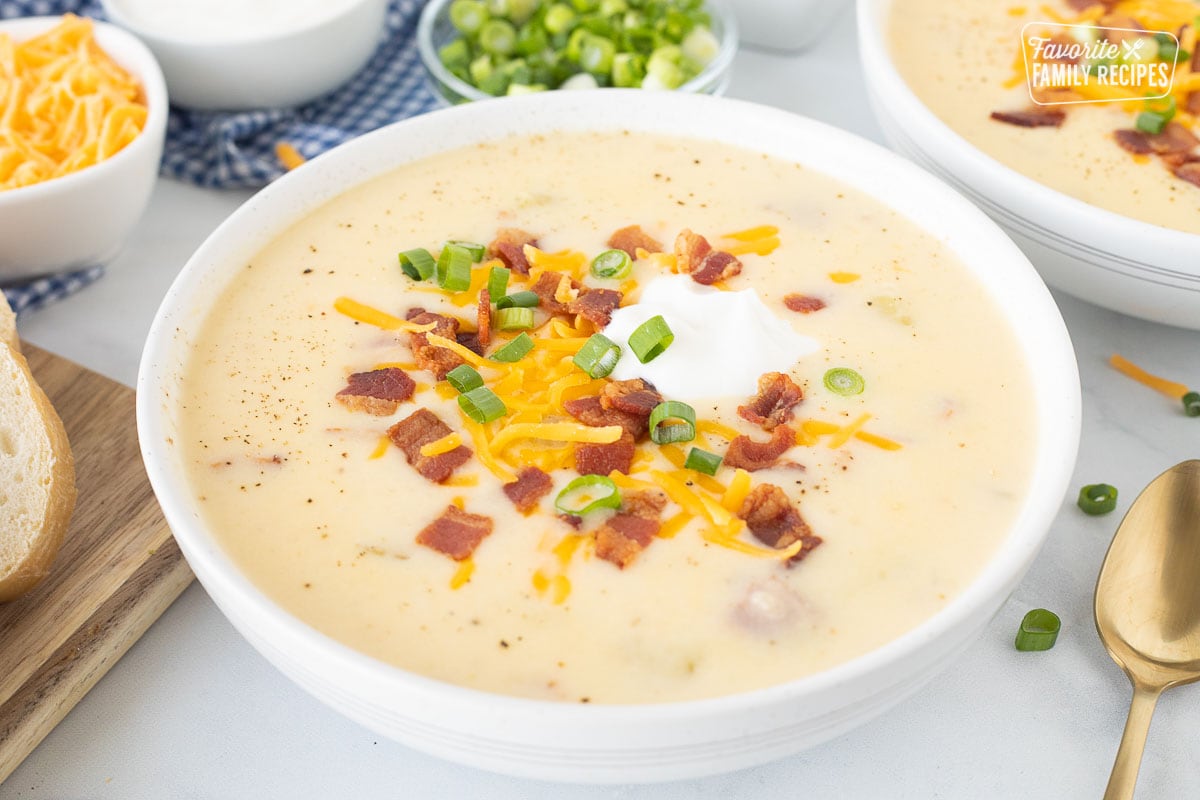 Close up of a bowl with Loaded Potato Soup garnished with cheese, sour cream, bacon and green onions.