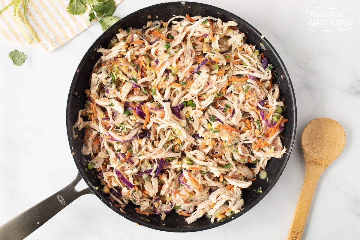 Skillet with chicken filling for Thai Chicken Enchiladas. Wooden spoon on the side.