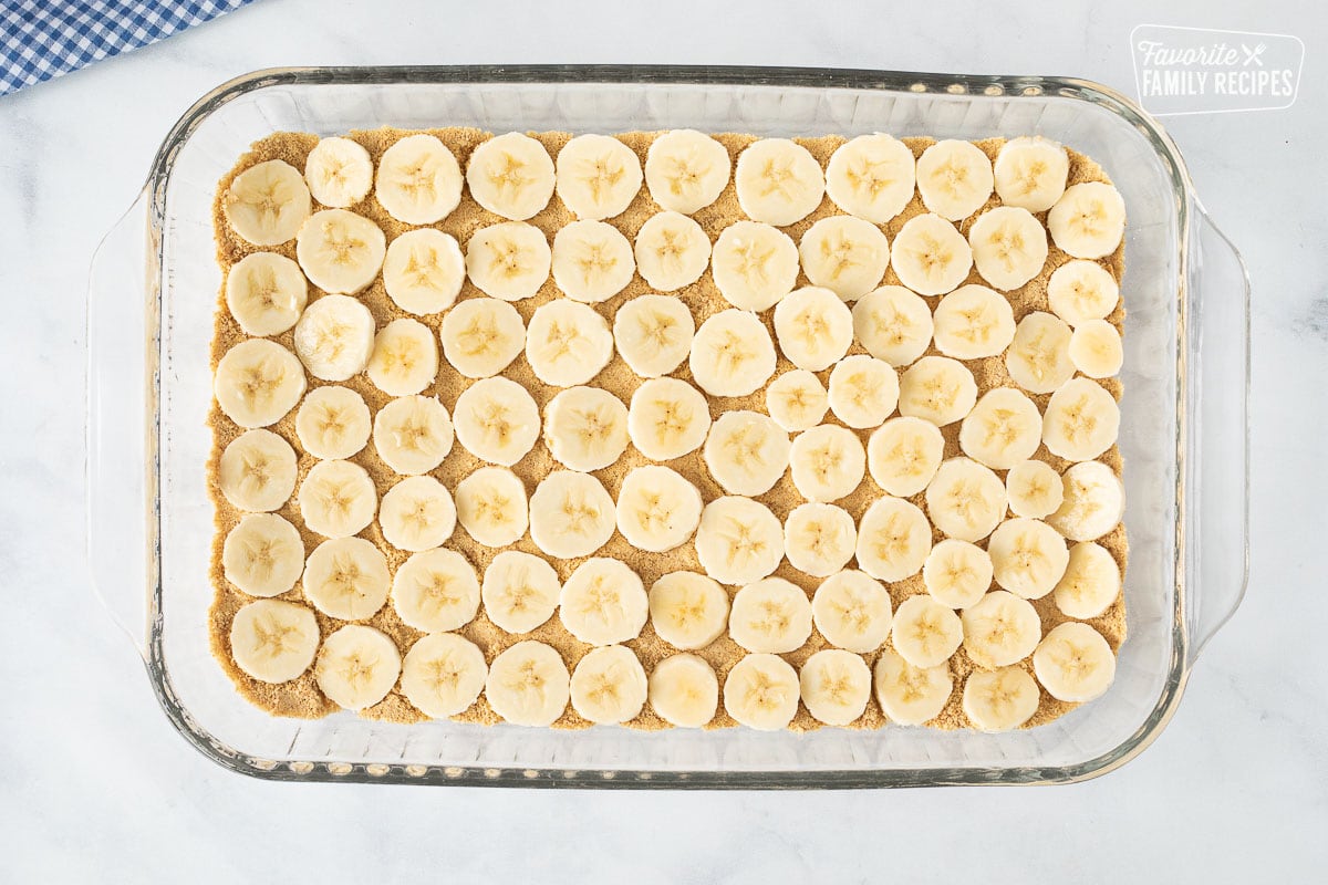 Glass rectangle with sliced bananas on top of graham cracker for Banana Split Dessert.