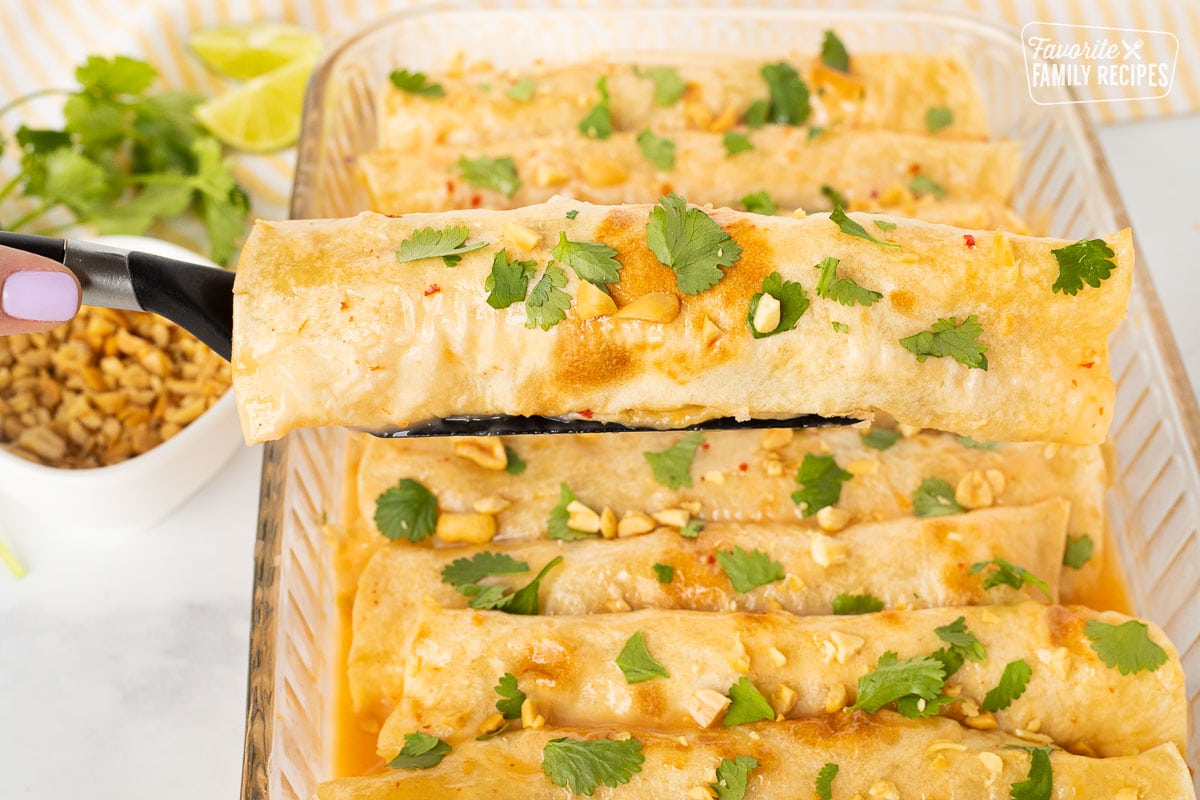 Dish of Thai Chicken Enchiladas with a spatula serving a single enchilada.