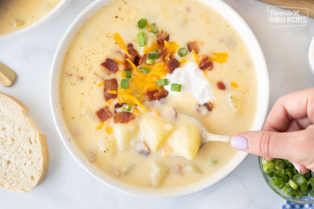Spoon scooping up Loaded Potato Soup with cheese, sour cream, bacon and green onions.