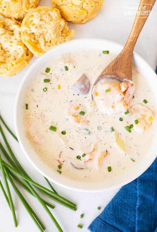 Spoon resting with a piece of shrimp in a bowl of Seafood Chowder. Biscuits on the side.