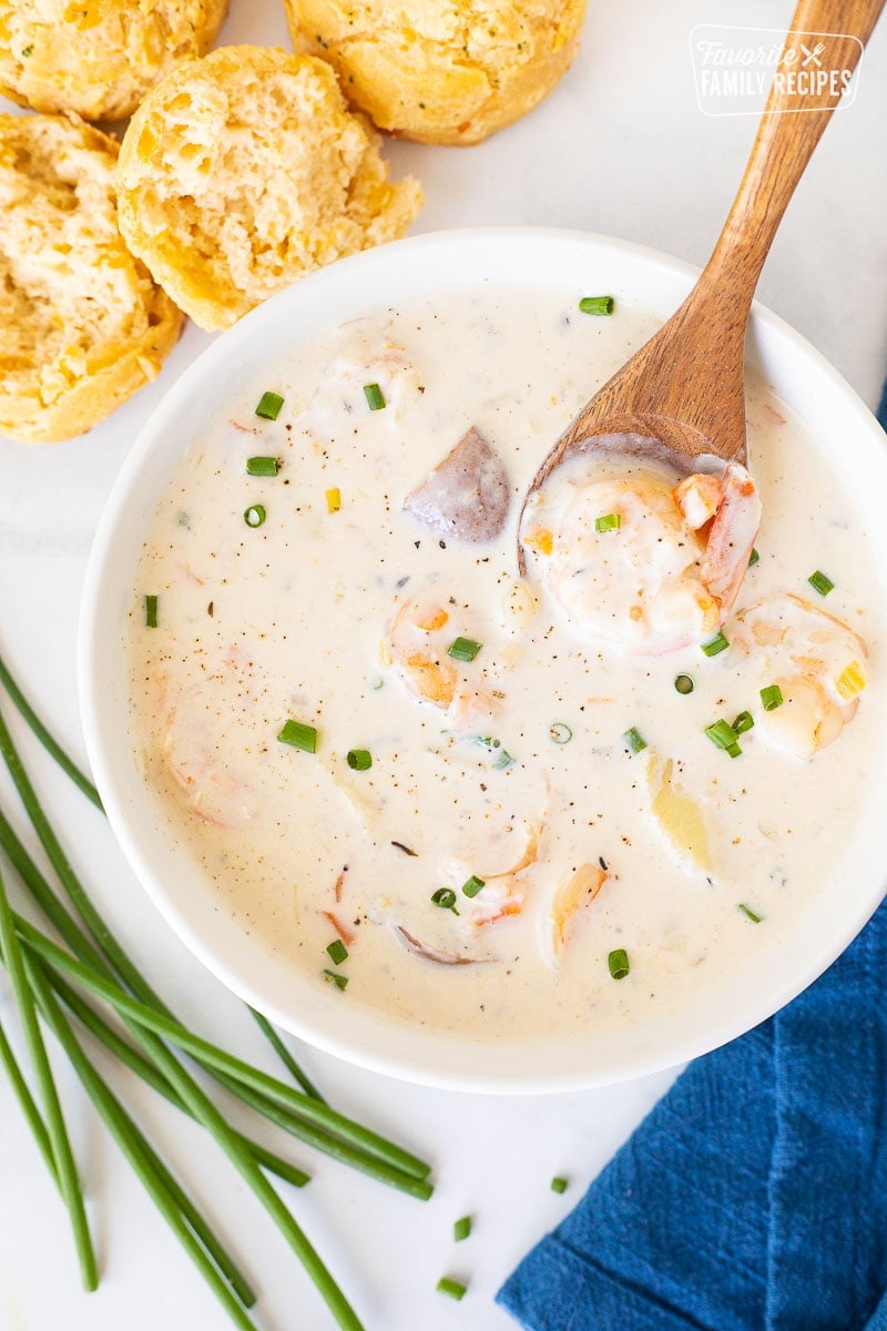 Spoon resting with a piece of shrimp in a bowl of Seafood Chowder. Biscuits on the side.