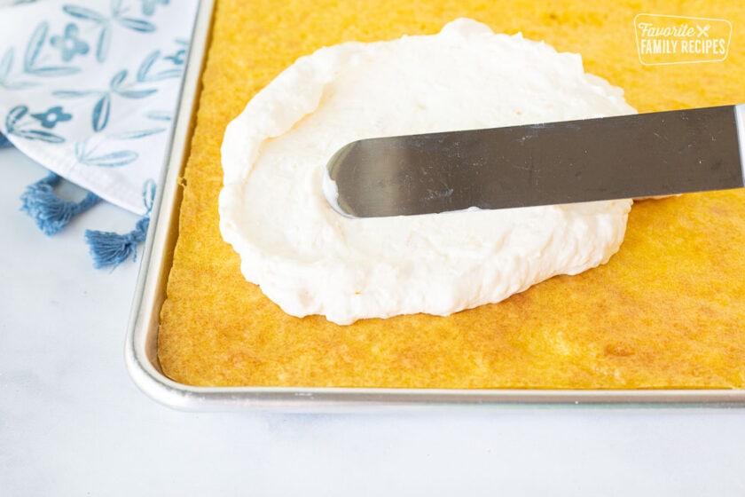 Spreading Pineapple topping with a spatula on top of a baked Orange cake.