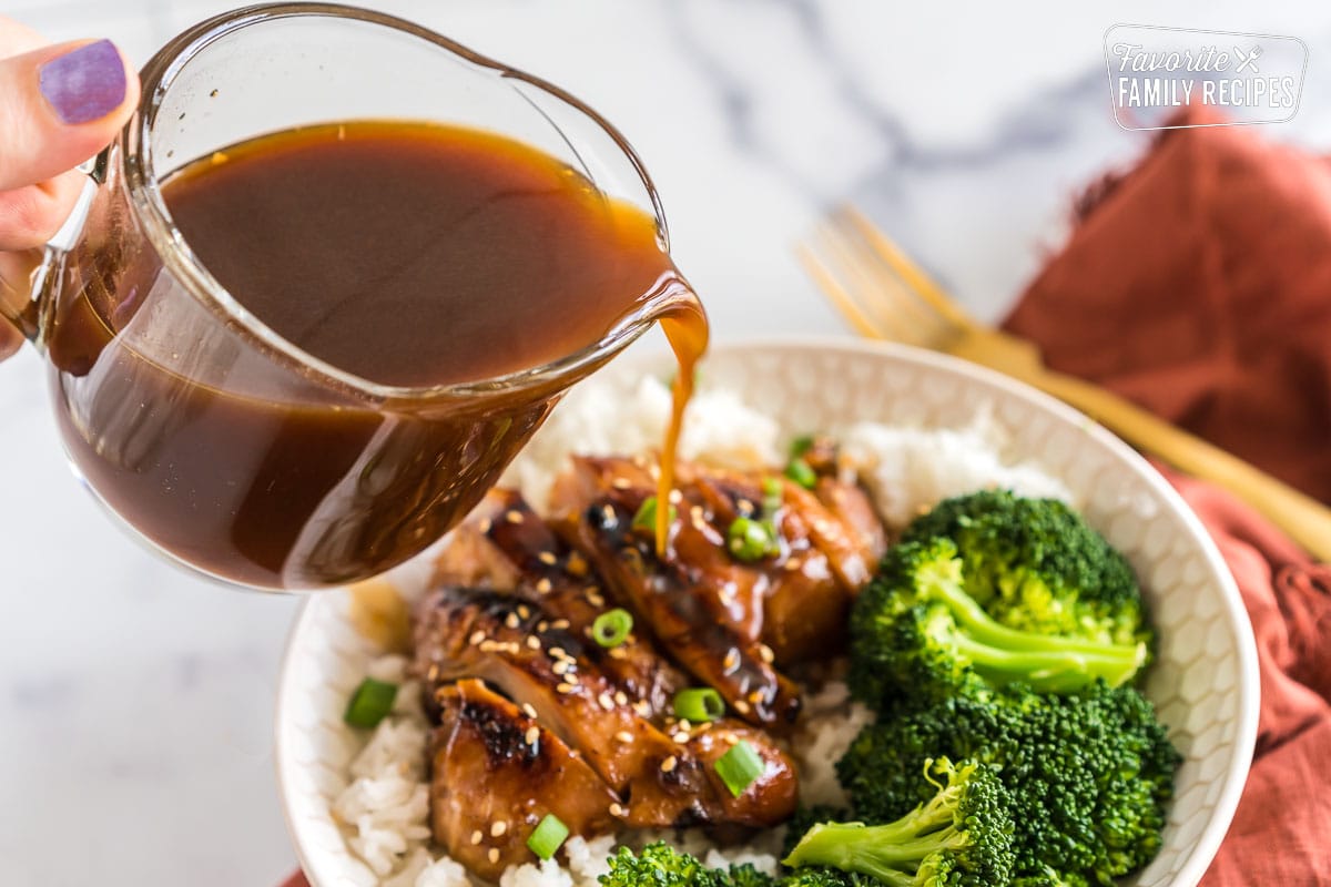 pouring teriyaki chicken marinade over a bowl of sliced chicken, broccoli, and rice