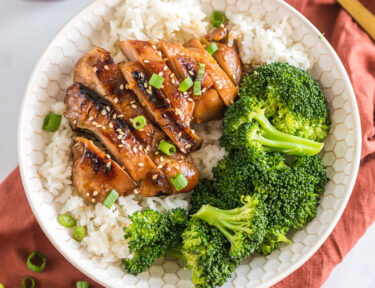 A bowl with rice, broccoli, and teriyaki chicken topped with sesame seeds and green onion