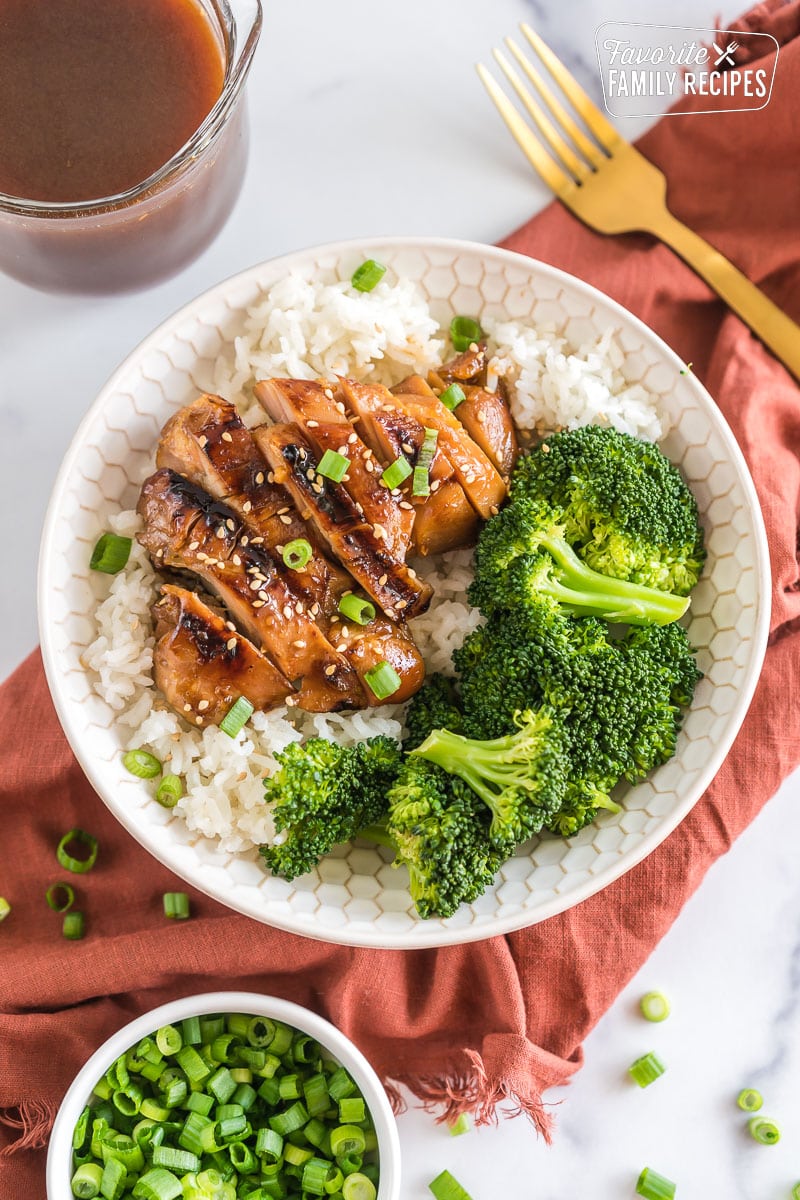A bowl with rice, broccoli, and teriyaki chicken topped with sesame seeds and green onion