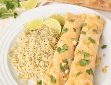 Two Thai Chicken Enchiladas on a plate with cilantro lime rice and fresh lime wedges.