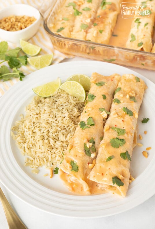 Two Thai Chicken Enchiladas on a plate with cilantro lime rice and fresh lime wedges.