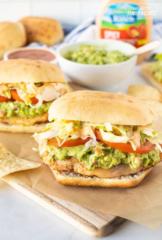 Chicken Tortas on a cutting board with guacamole, lettuce, tomatoes and spicy ranch.