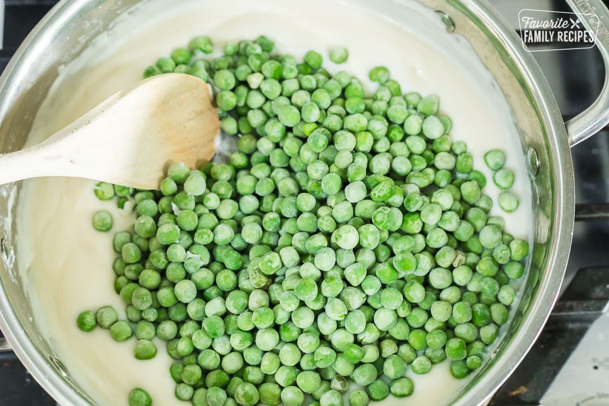 Frozen peas being stirred into a cream sauce to make creamed peas
