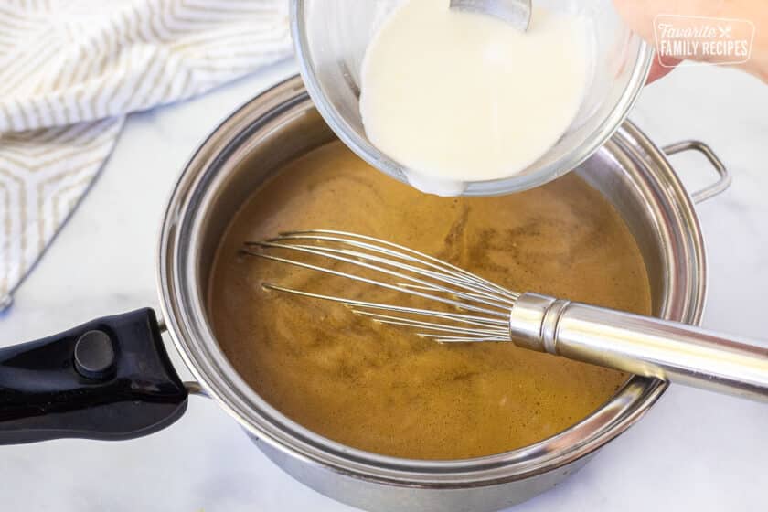 Adding corn starch slurry to the pan of Beef Gravy with a whisk.