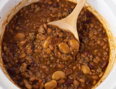 Wooden spoon rising in a Crockpot of Baked Beans.