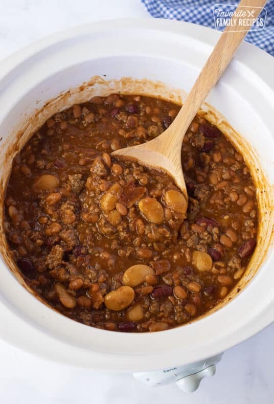 Wooden spoon rising in a Crockpot of Baked Beans.