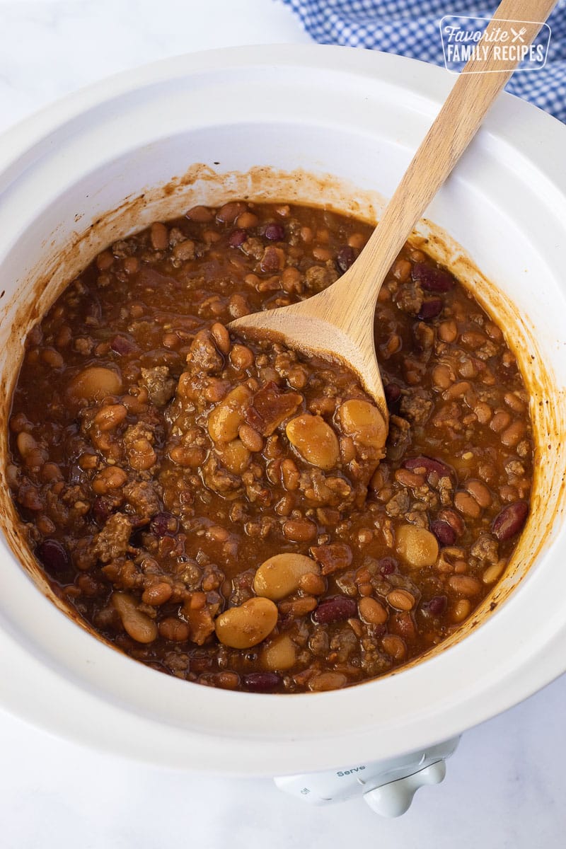 Wooden spoon rising in a Crockpot of Baked Beans.