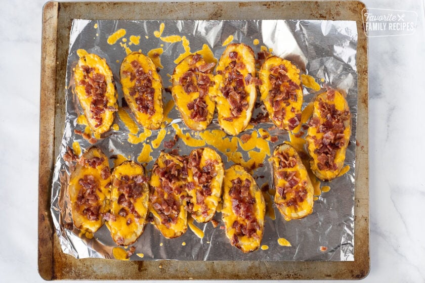 Cookie sheet with twelve melted Potato Skins with cheddar cheese and bacon on top.