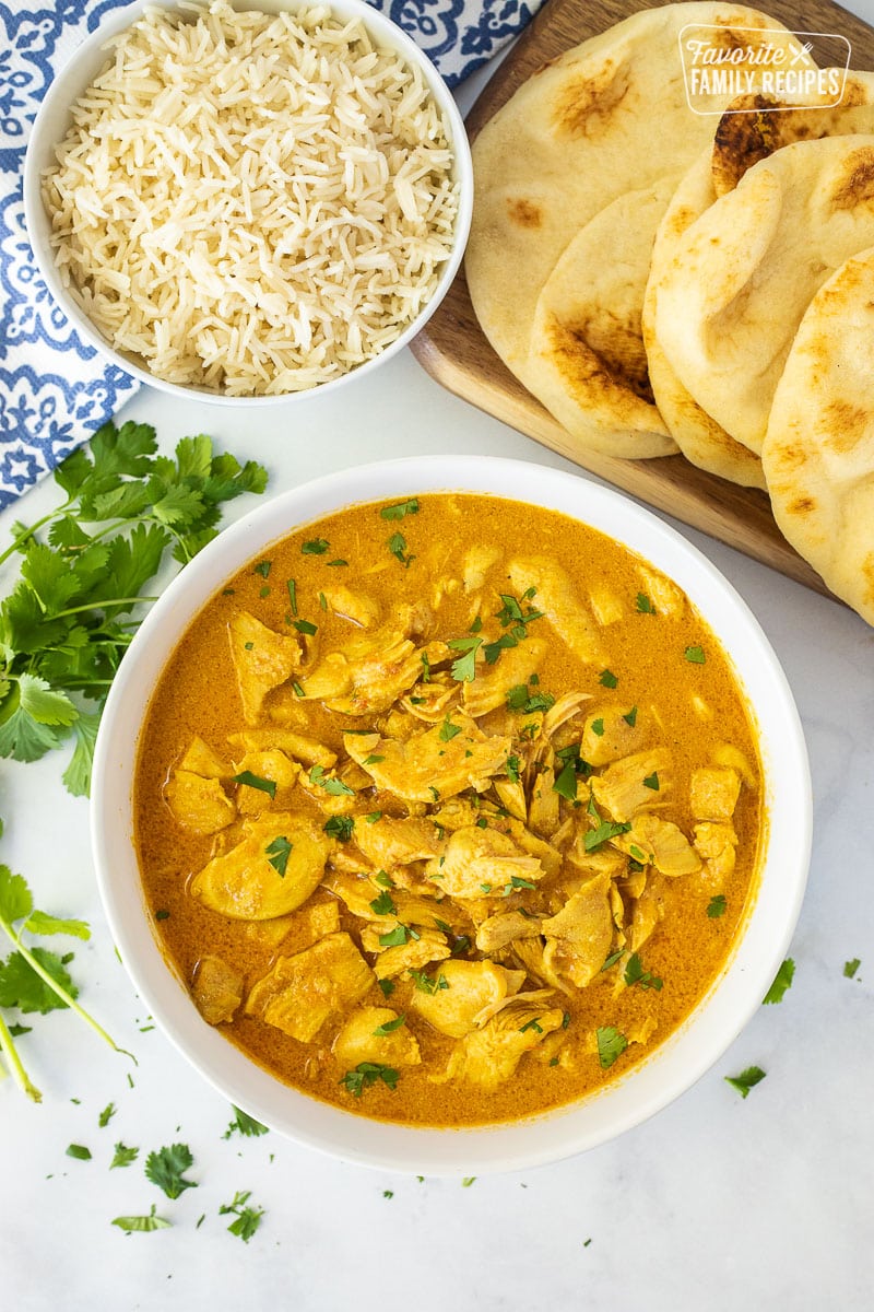 Bowl of Chicken Korma topped with chopped cilantro. Rice and Naan Bread on the side.