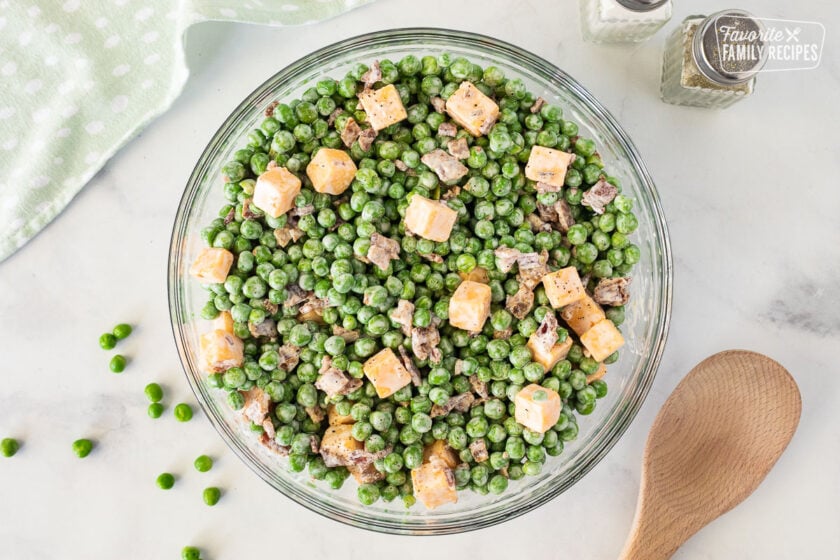Glass Bowl of Green Pea Salad with a wooden spoon on the side.