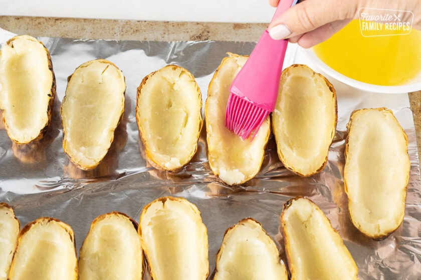 Hand brushing butter onto Potato Skins on a cookie sheet covered with foil.